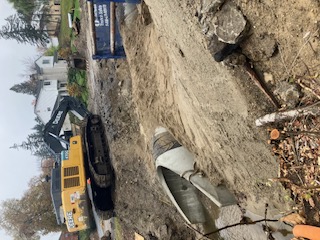 Excavator placing concrete pipe in trench during backfill.